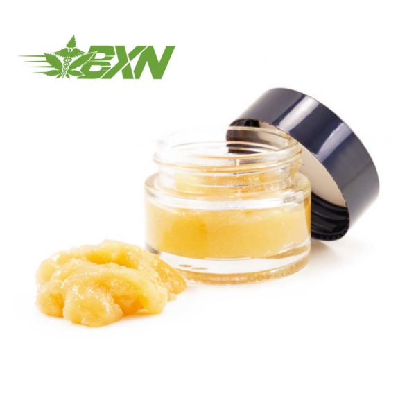 A small glass jar filled with yellow paste-like substance, partially open with some of the substance scooped out and placed beside the jar. Green "BXN" logo in the corner of the image.